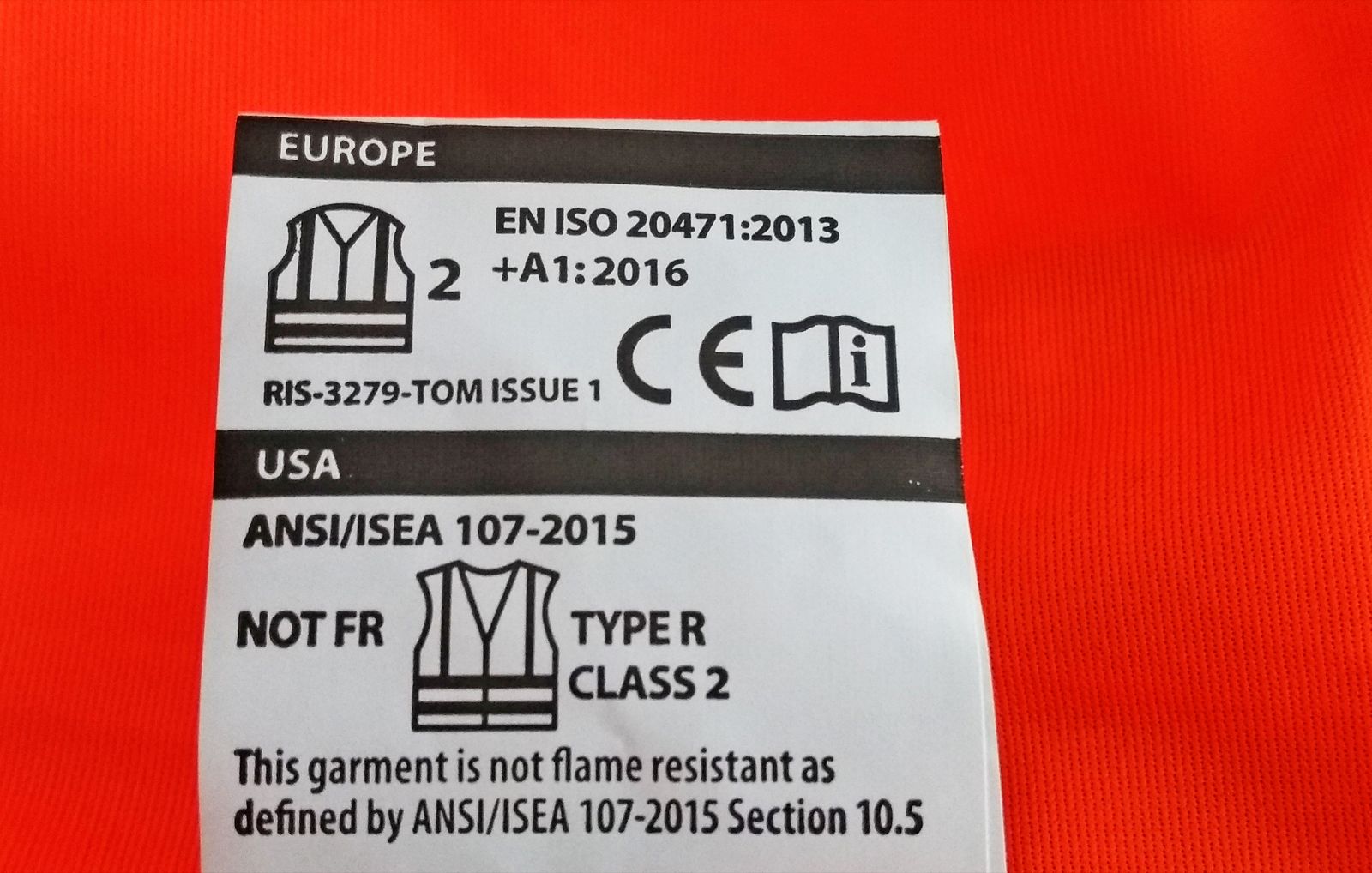 Etiqueta blanca cosida a un chaleco naranja fluorescente con el pictograma del chaleco, el número 2 de la clase, la referencia EN ISO 20471 y el marcado CE