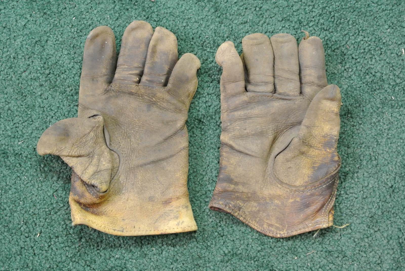 Par de guantes de trabajo de piel, muy usados y ennegrecidos, sobre una moqueta verde