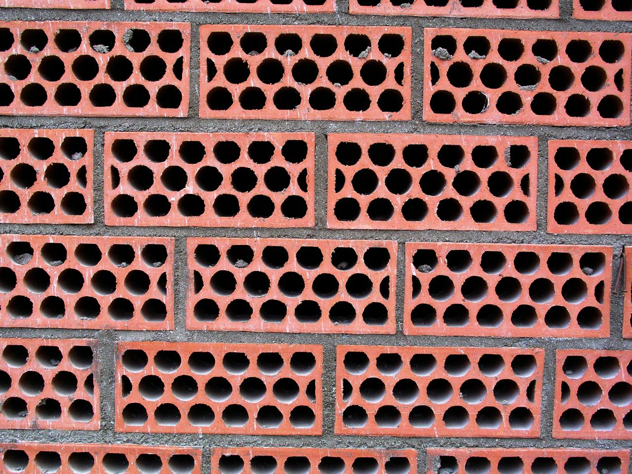 Pared de ladrillo perforado rojo con muchos agujeros redondos a la vista, con juntas de mortero gris