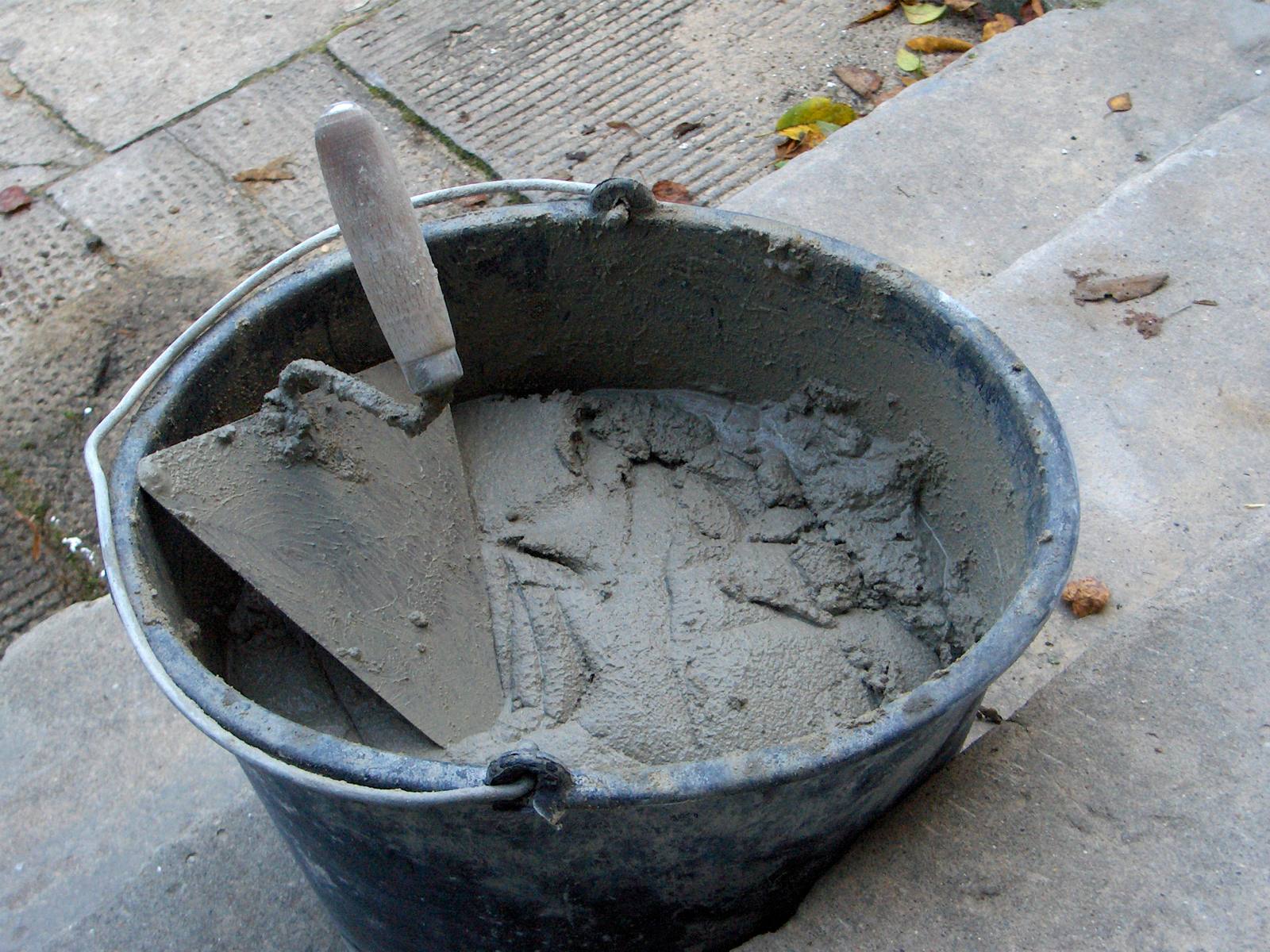 Cubo de goma negro con mortero de cemento recién amasado y una paleta metida en la mezcla