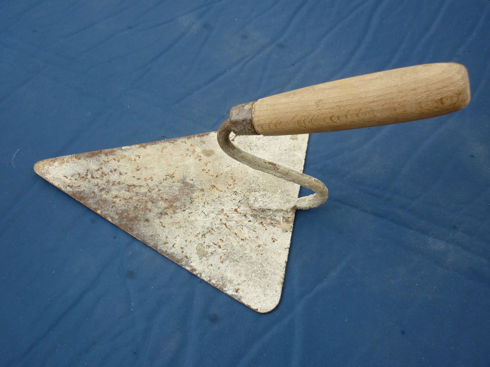 Paleta de albañil de hoja triangular y mango de madera, gastada por el uso, sobre una lona azul